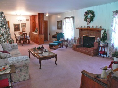 Alternate view of living room with front door entrance, gas and wood-burning brick fireplace.