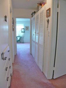 Long hallway connecting two bedrooms on left side of the house. Deep linen closet to the left and organized shelving behind levered doors on the right.